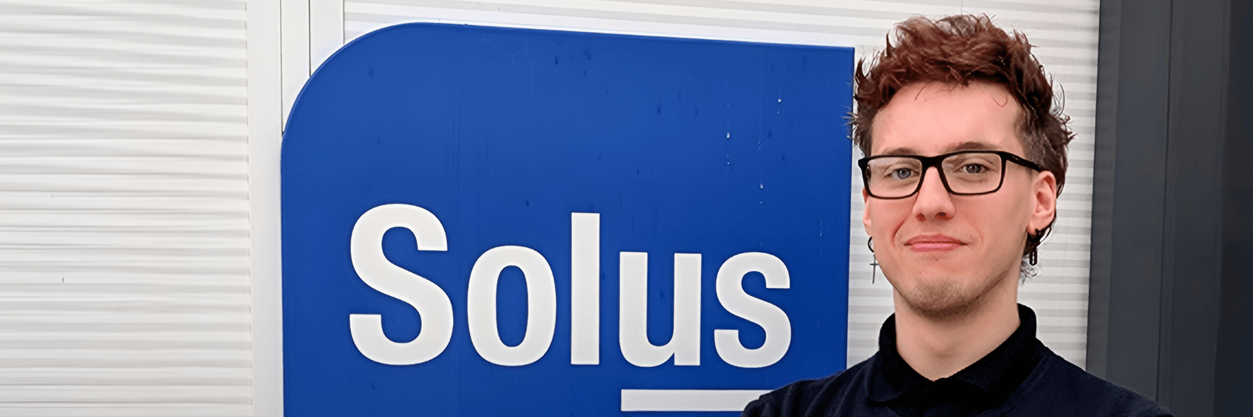 A confident employee standing with arms crossed in front of the Solus sign.