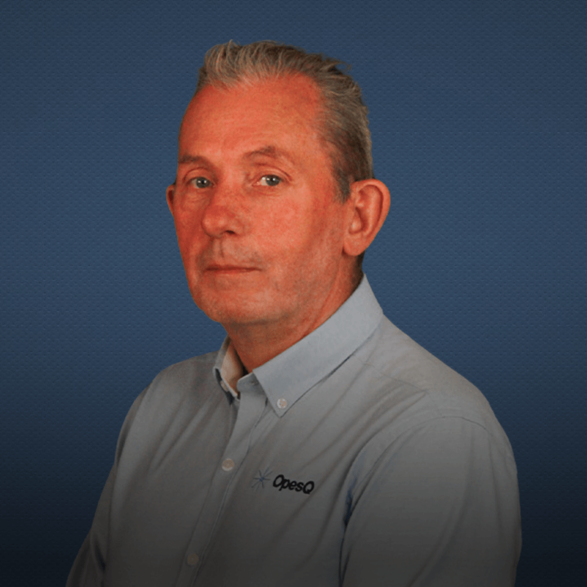 Professional portrait of a man wearing a light blue button-up shirt with the "OpesQ" logo, set against a textured dark blue background.